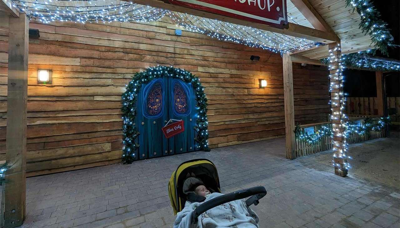 A baby in a pram in front of the Christmas shop.