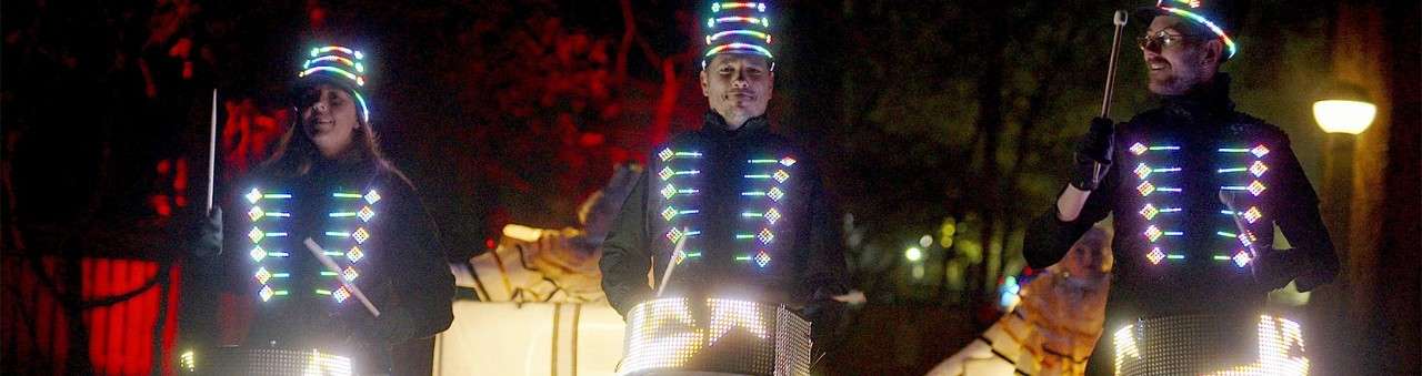 Drummers with lit up costumes walking through Santa's Woodland Village.