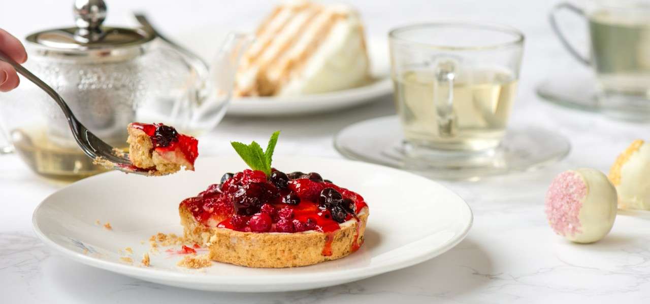 A berry tart on a plate surrounded by afternoon tea items.