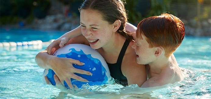 Brother and sister playing together with an inflatable ball in the swimming pool in The Subtropical Swimming Paradise.