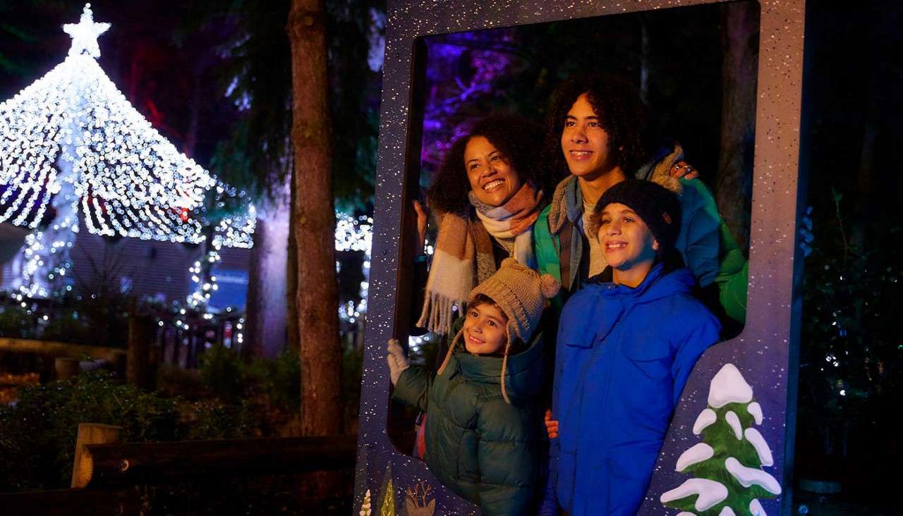 A family posing for a photo behind a giant photo frame in the forest.