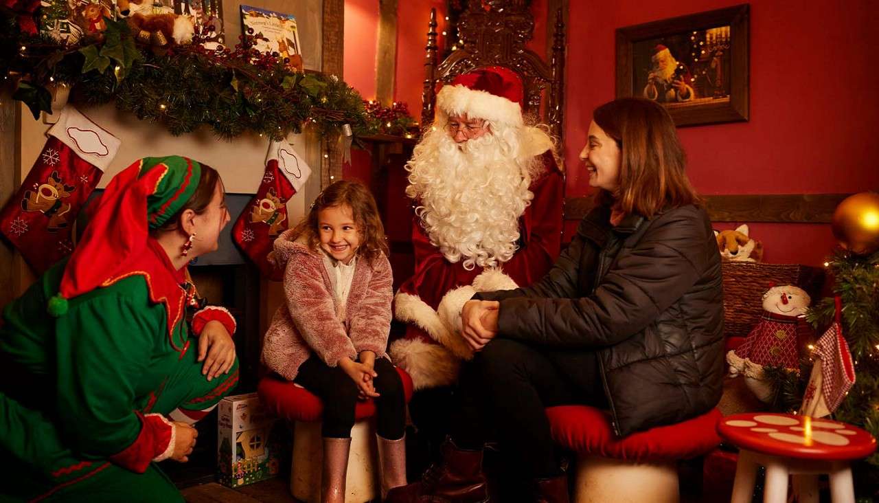 A little girl sat next to father Christmas talking to an elf.