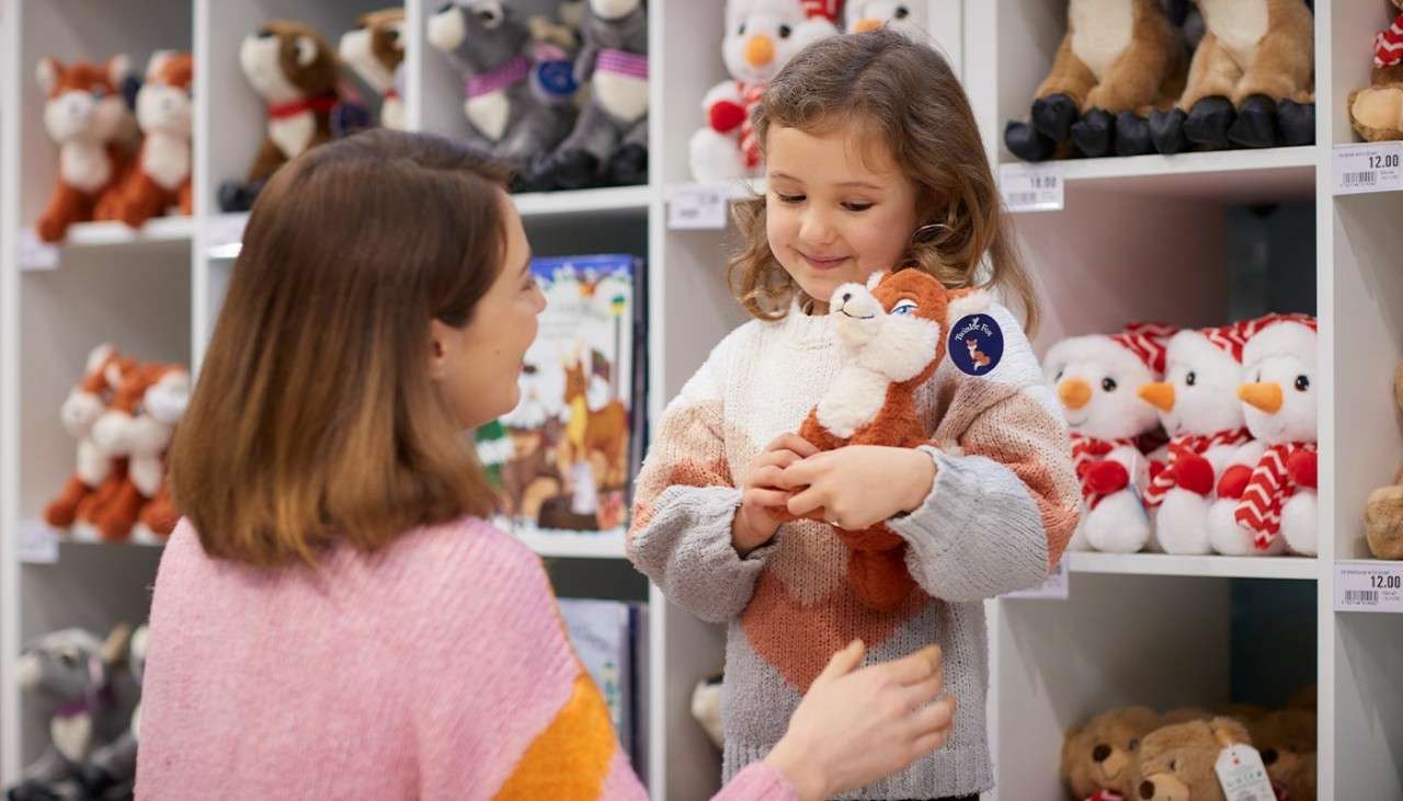A little girl holding a plush fox toy in a Christmassy shop.