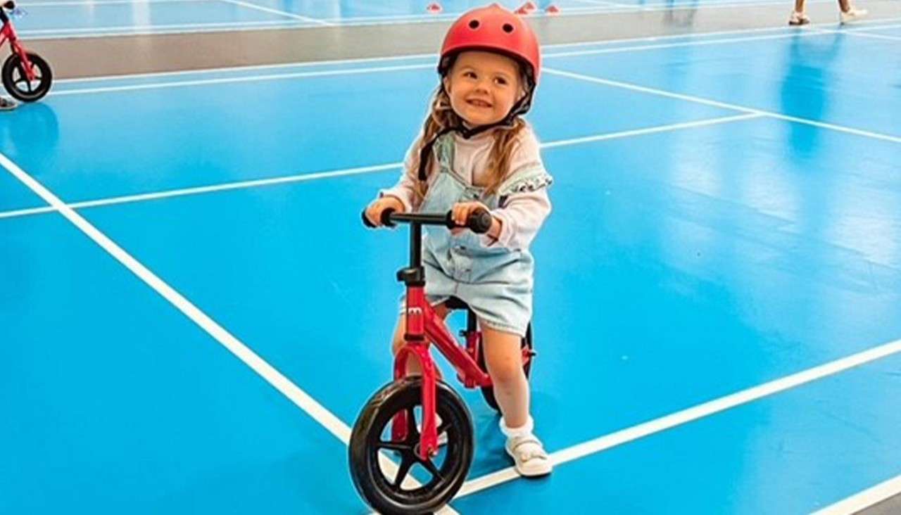 A little girl on a balance bike inside the Sports Plaza. 