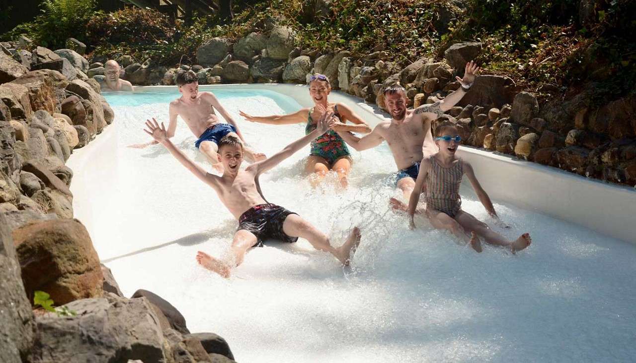 A framily of five sliding down the rapids with their arms in the air. 