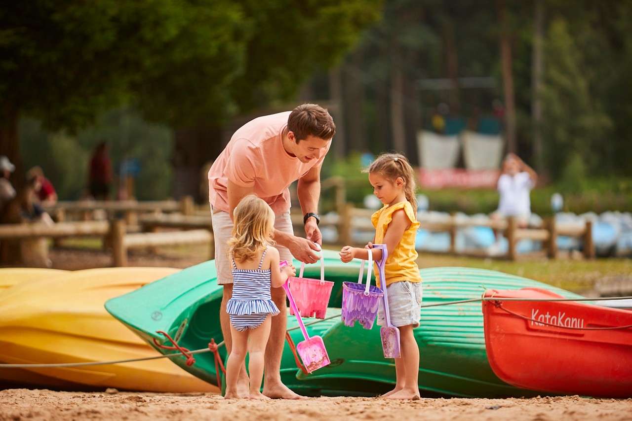Child in a yellow sleeveless top smiles and looks right, standing in sunlit woodland with blurred trees and dappled light.