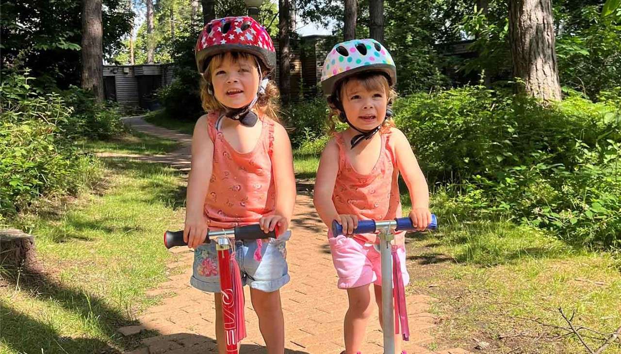 Two toddlers on their scooters in the forest.