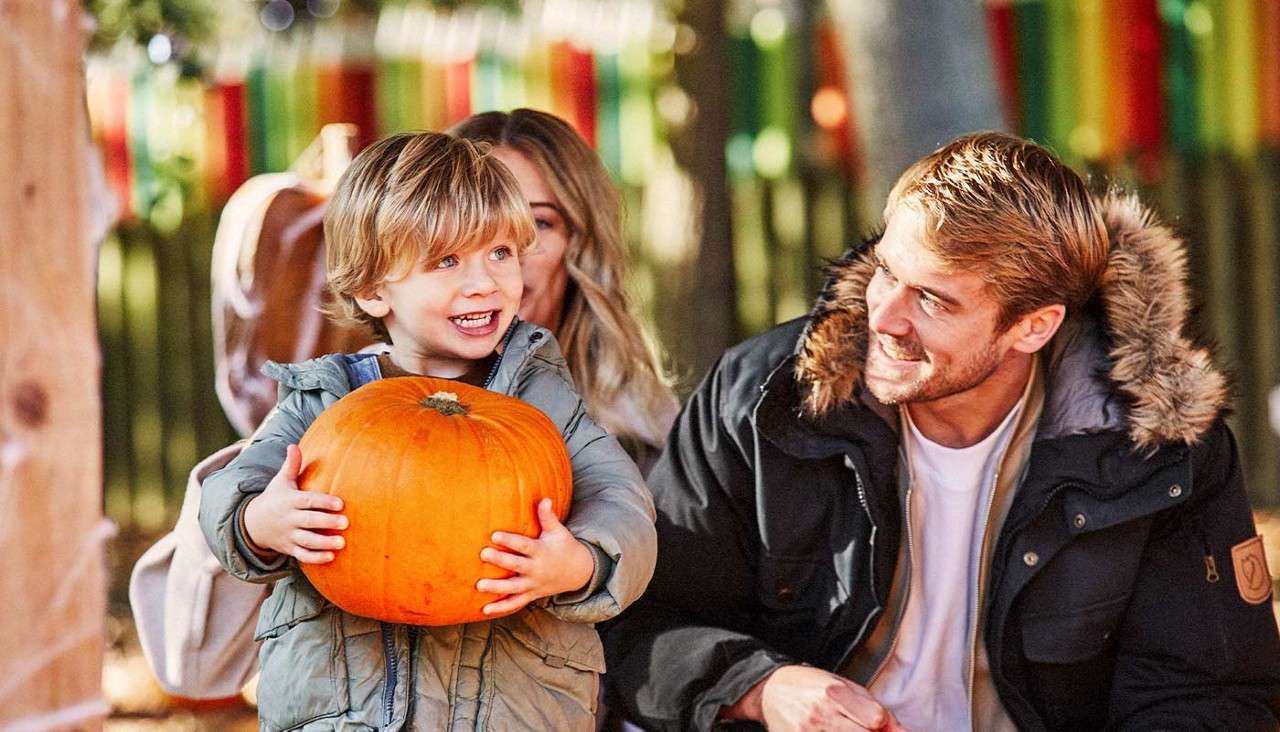 A young boy carrying a large orange pumpkin.