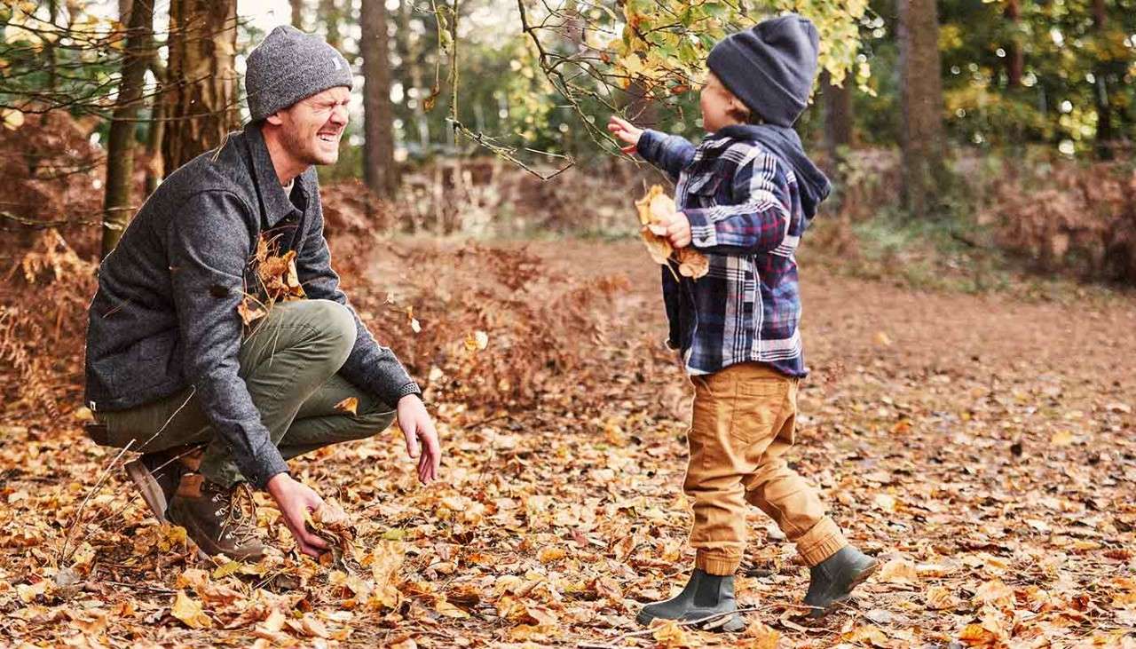 A father and son laughing in the leaves on a woodland walk.