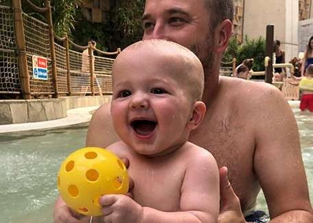 Baby playing with a ball in the pool with father