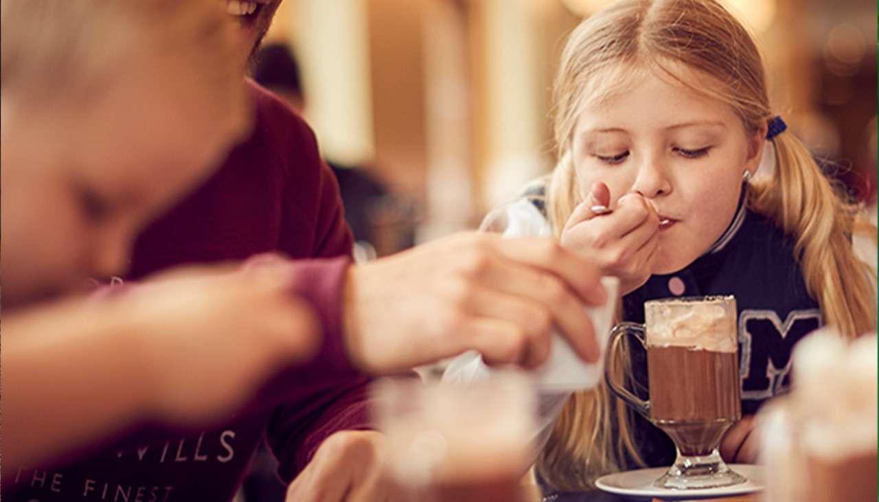 A little girl eating the cream from a hot chocolate.