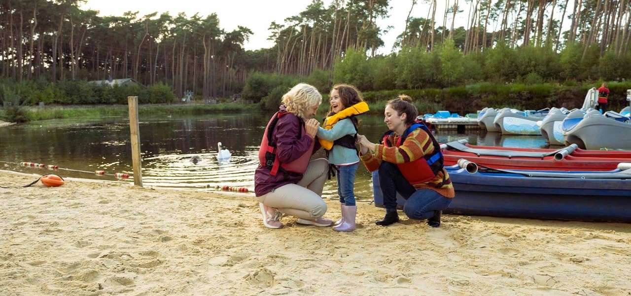 A grandma and mother on a beach helping a little girl to put on a lifejacket.