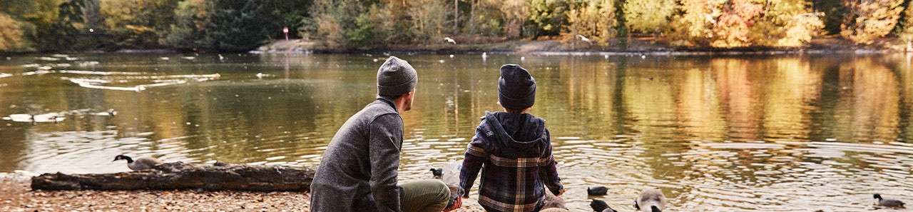 A father and his son looking out at the autumn lake whilst feeding ducks.