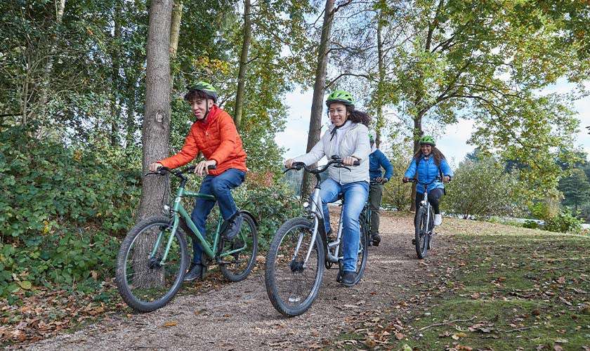 A family cycling through the forest next to the lake.