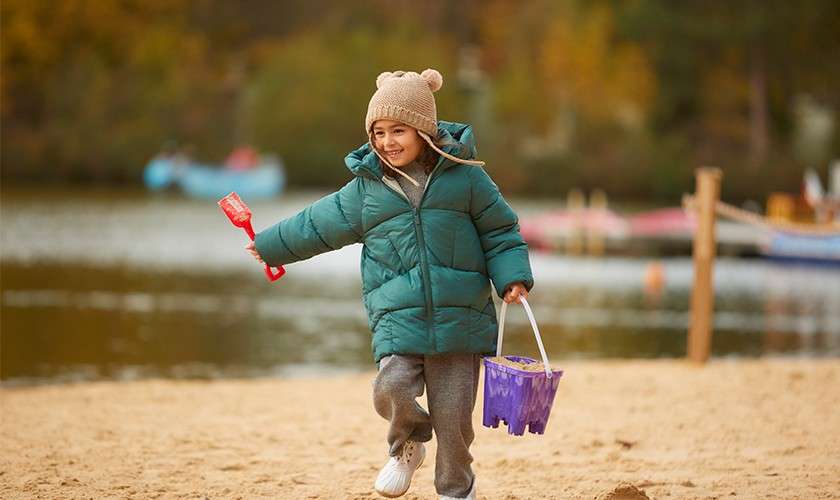 A little girl running across the beach with a bucket and spade