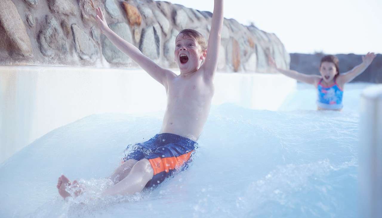 A boy sliding down the rapids waving his arms in the air. 