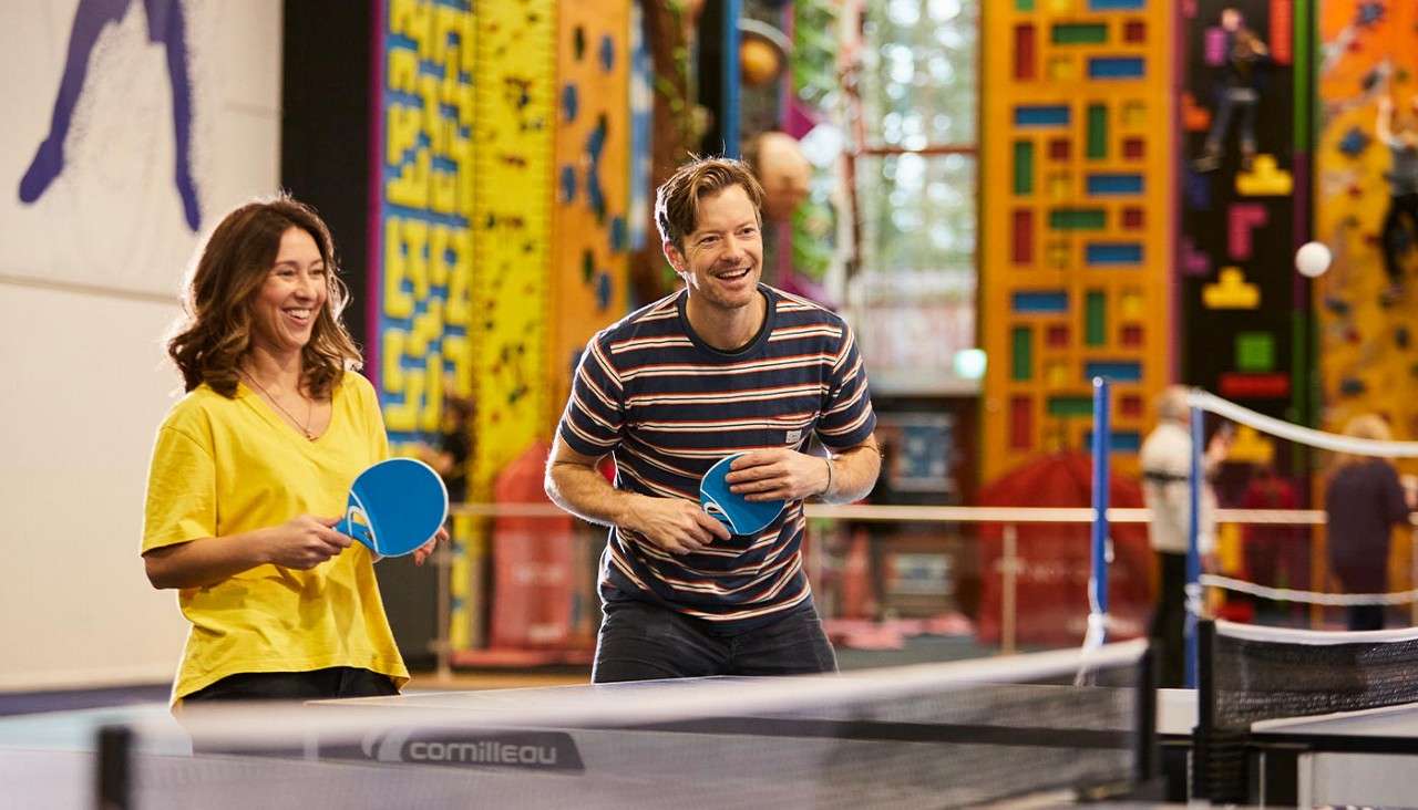 A couple laughing and playing indoor table tennis.