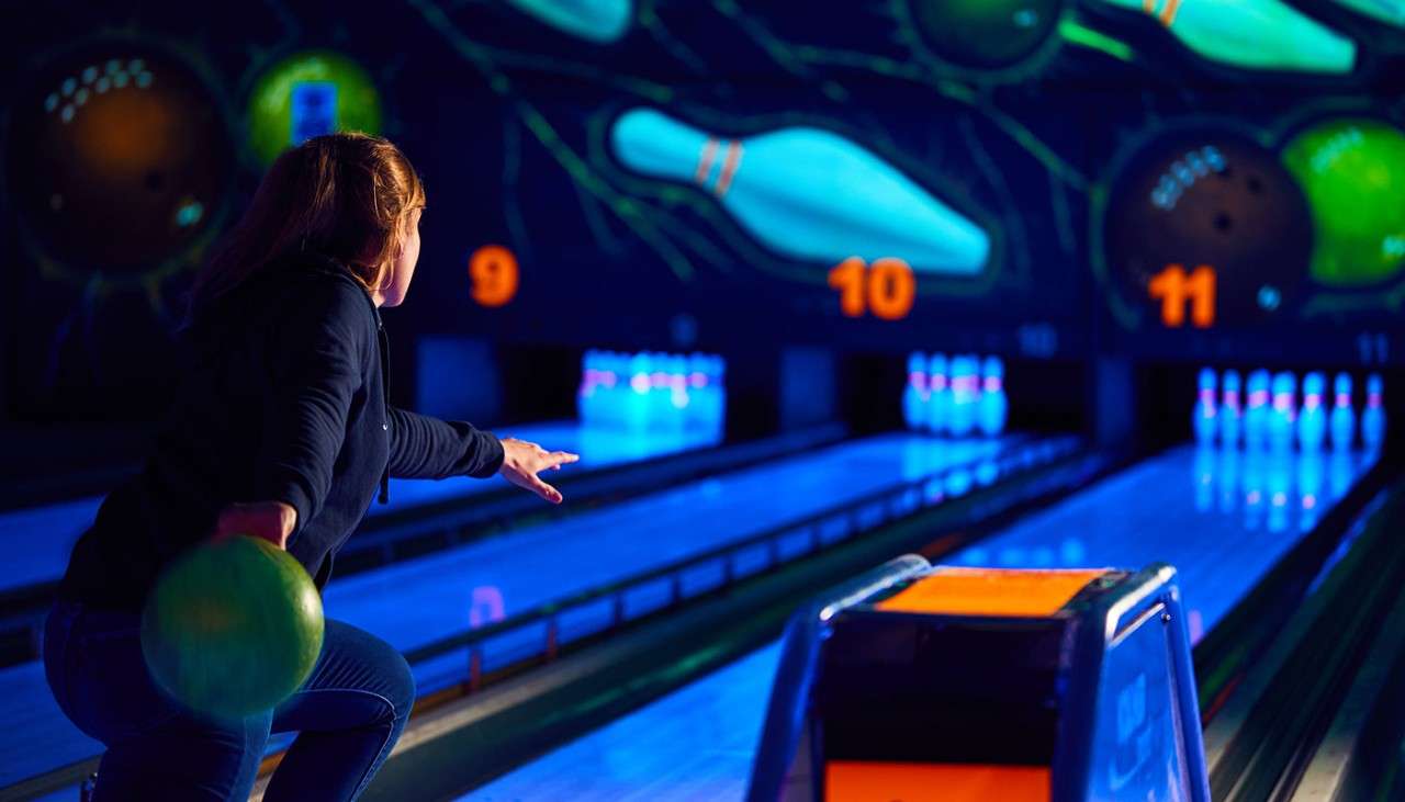 A girl throwing a bowling ball down the lane and everything is glow in the dark.