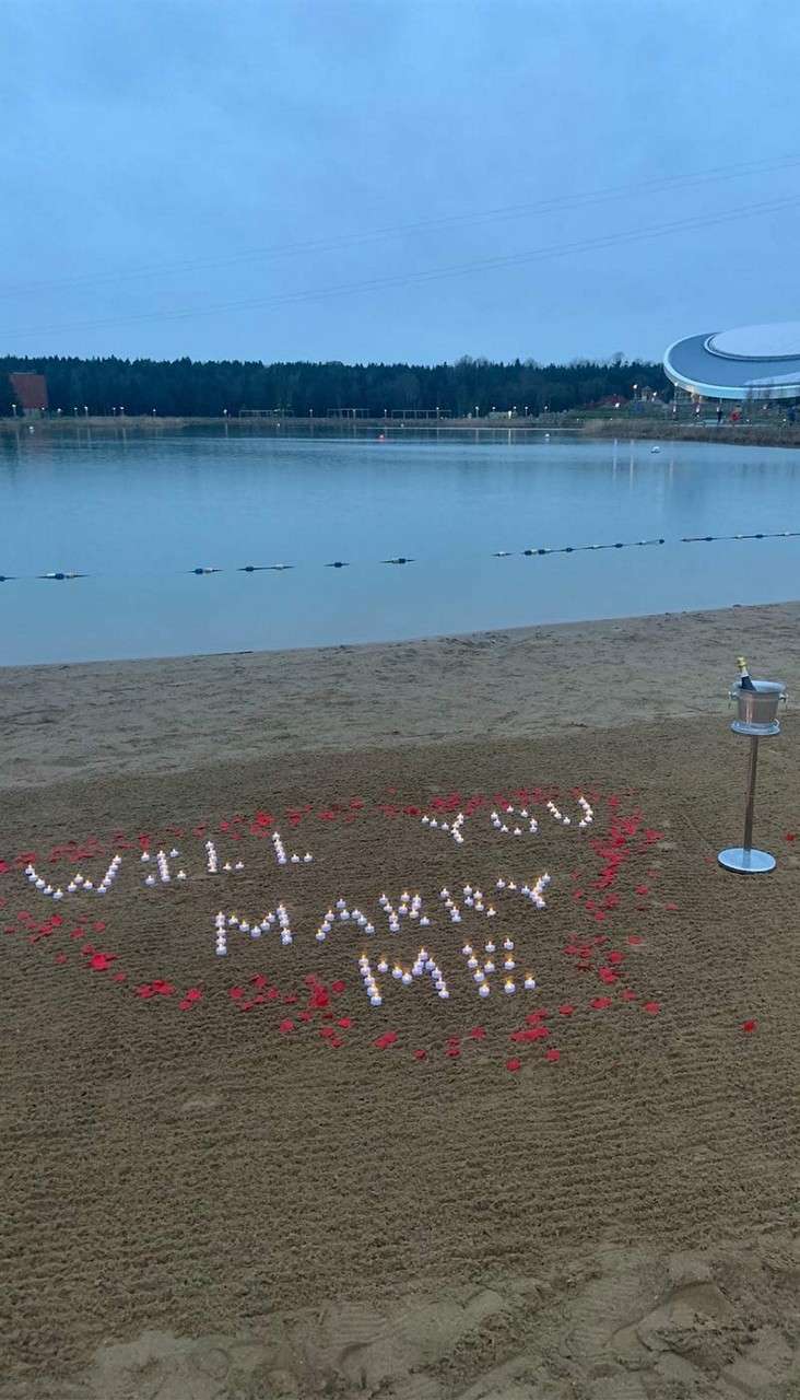 "Will you marry me" written on the beach with stones with a bottle of champagne in an ice bucket.