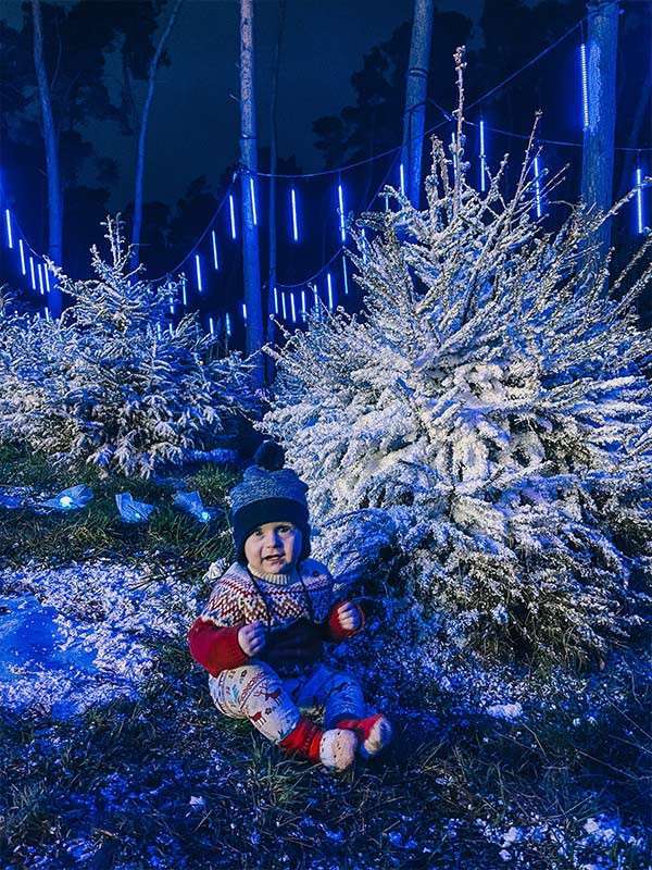 A baby sat in front of a Christmas tree.