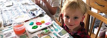 A little girl sat at a table doing arts and crafts.