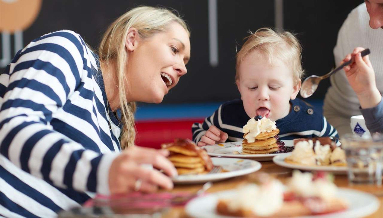A toddler and mother with plates of pancakes in front of them.