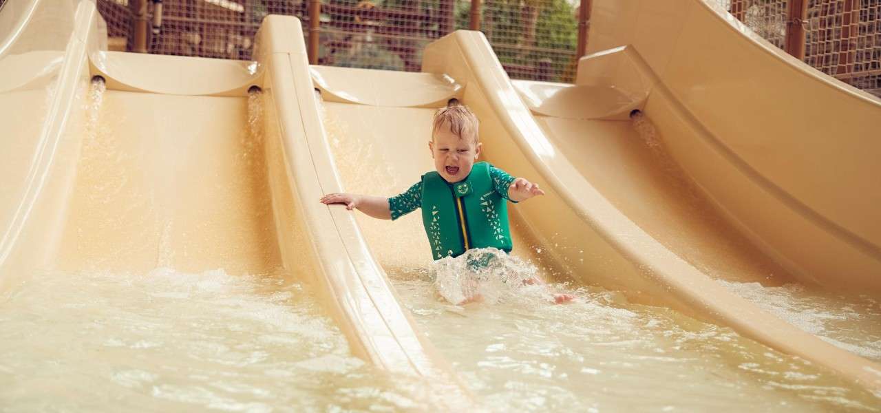 A toddler wearing a life jacket sliding down a small waterslide.