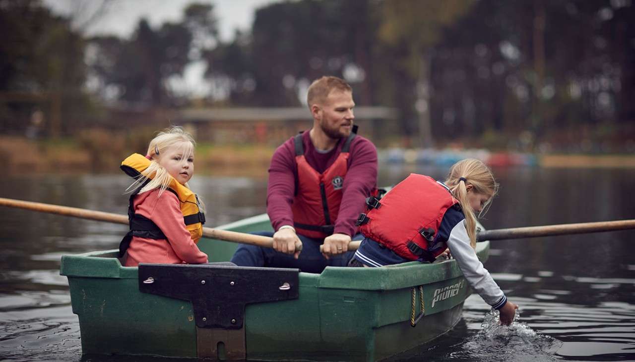 Father and two daughters on rowing boat on lake.