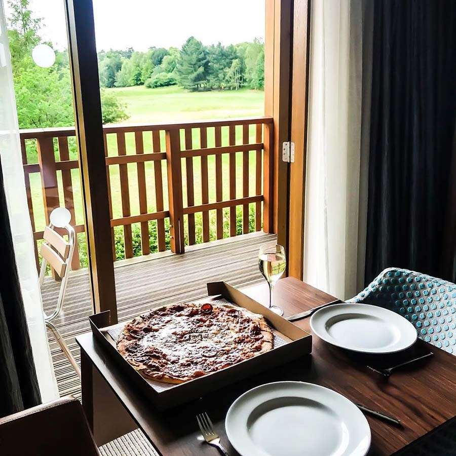 Table set up with pizza and wine in a Center Parcs apartment, showing a beautiful forest view from the balcony.