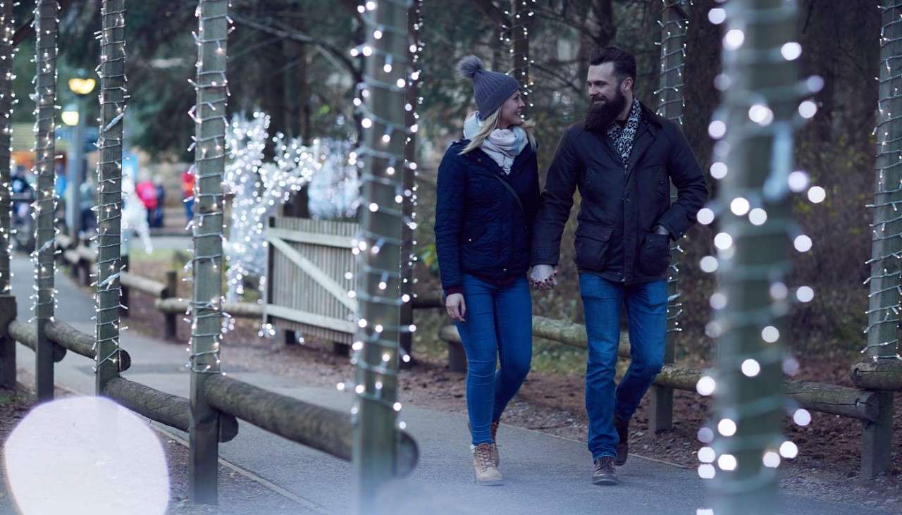 Couple holding hands as they walk through Winter Wonderland where the pathway is decorated with Christmas lights.