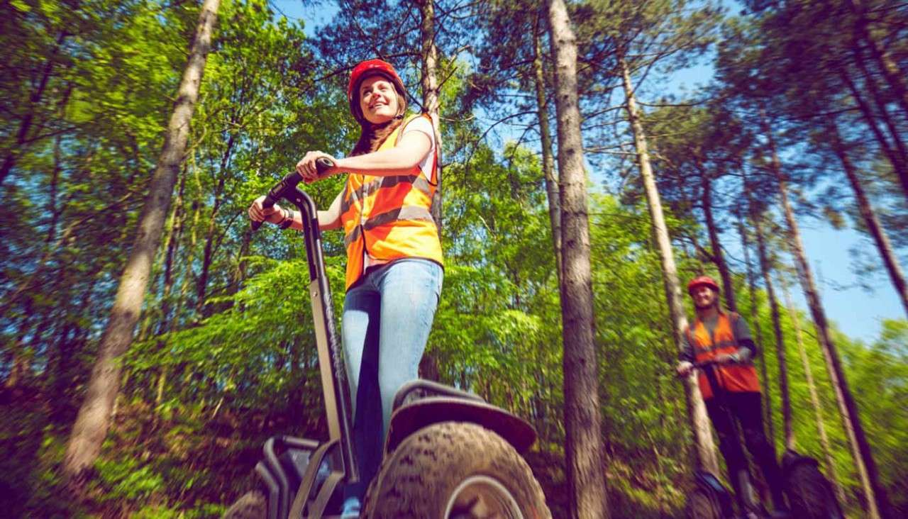 Two adults on a segway in the forest.