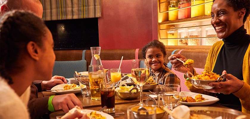 A family sat around a table at a restaurant eating Indian food..
