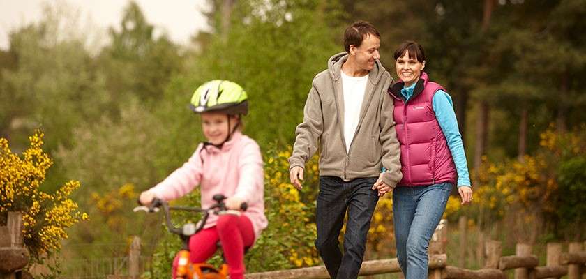 Mother and Father walking down a path while their daughter rides a bike