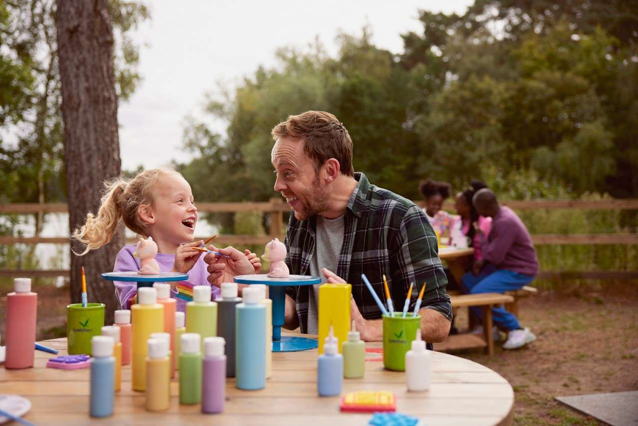 Girl with an adult painting pottery outside.