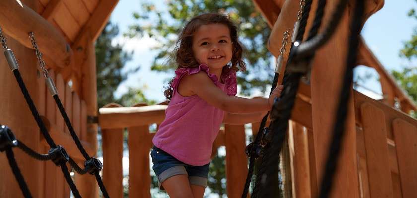 Young girl walking across a rope bridge on an outdoor play area.