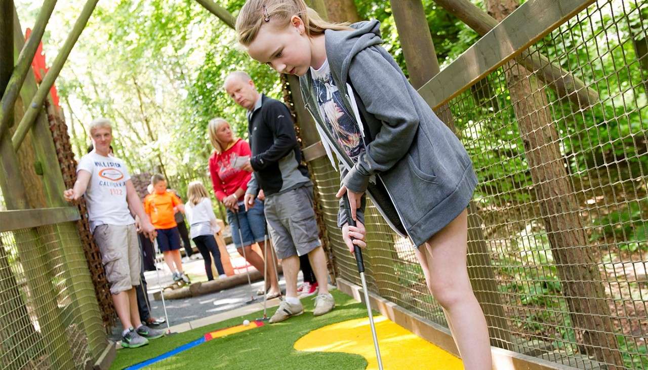 Young girl playing Adventure Golf as her family watch.