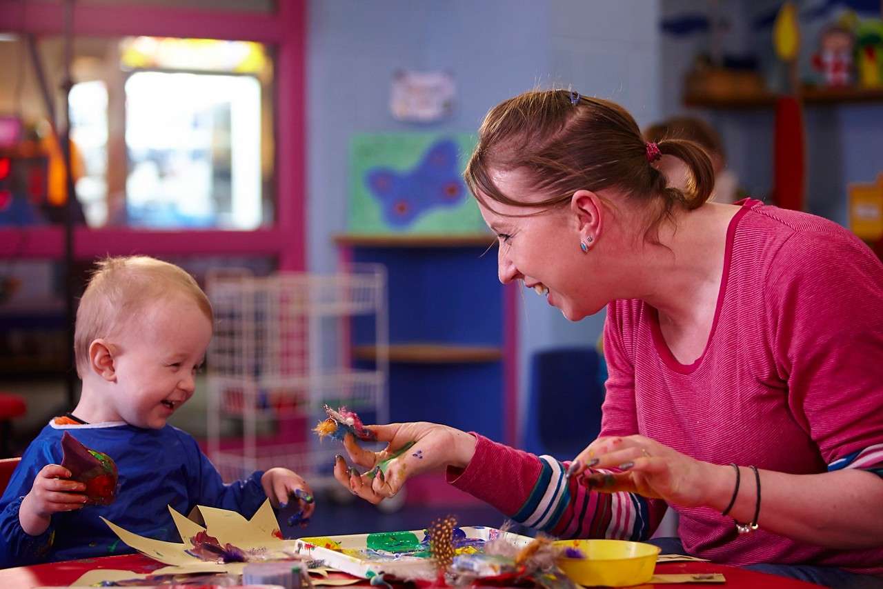 Infant sitting whilst they enjoy some messy crafts with an adult.