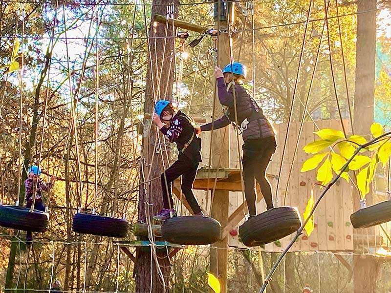 Man helping a young person across a suspended tire bridge.