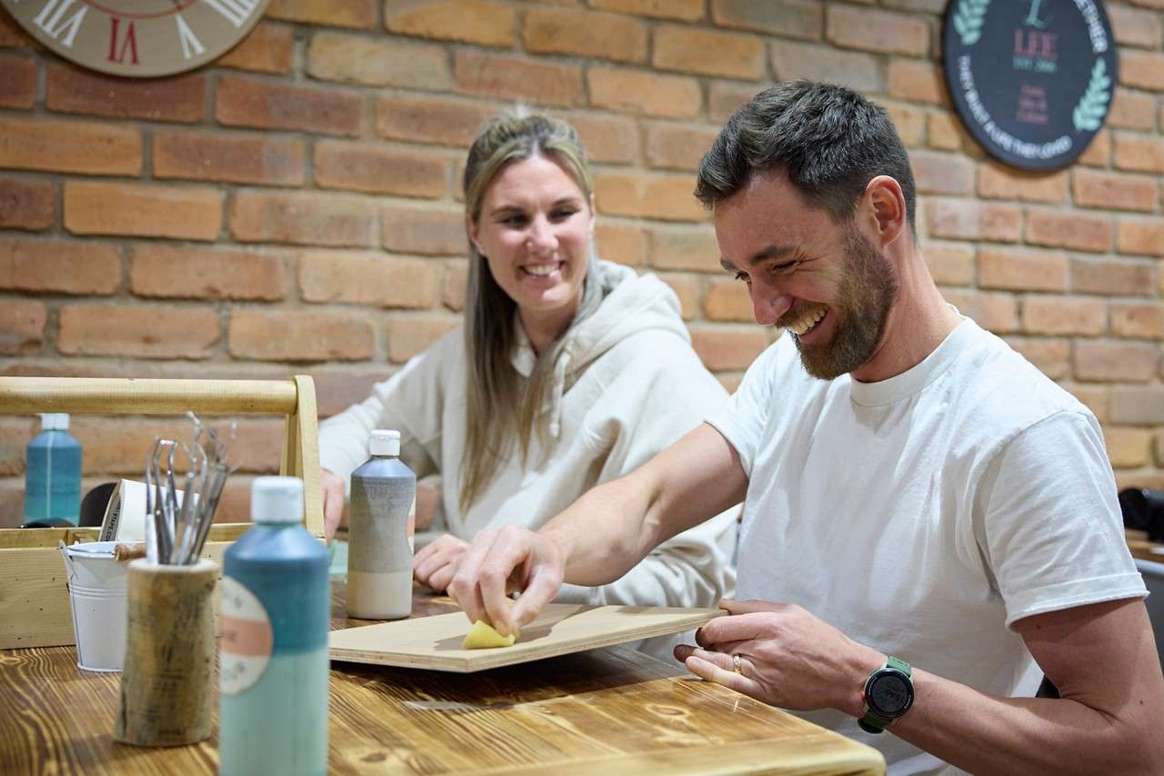 Two adults painting wooden plaques.