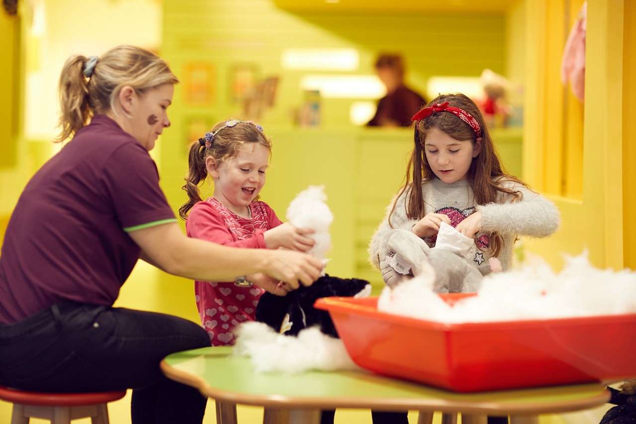 Two young girl making teddy bears with an adult.