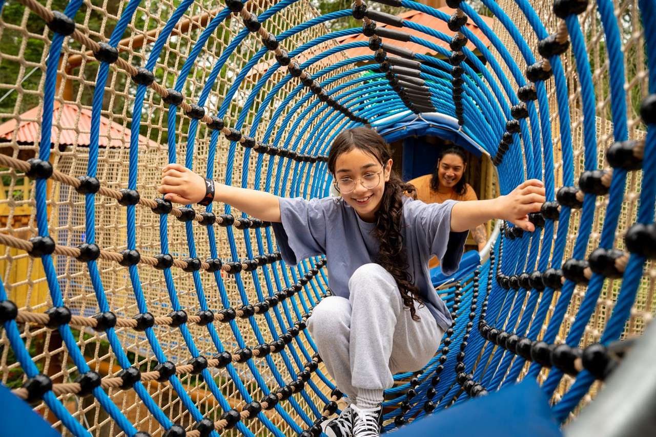 A teenage girl crawling through the Adventure Nets smiling. 
