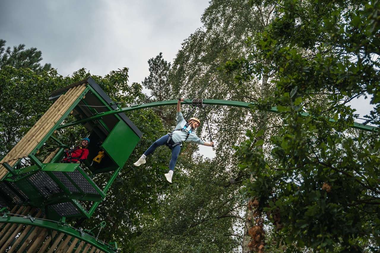 Woman suspended from a metal track that runs through the forest.