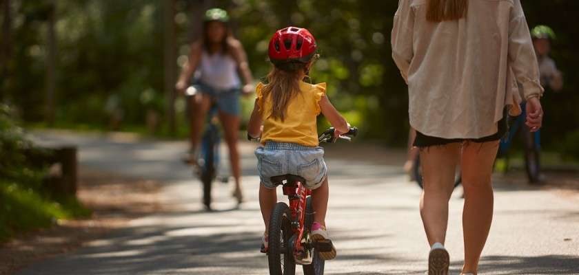 Young girl cycling beside a woman walking through the woods.