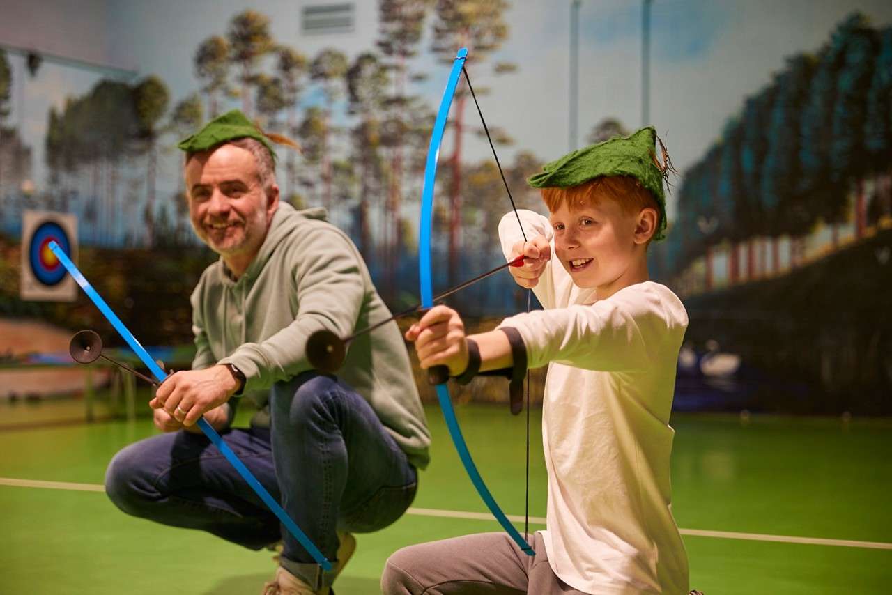 Boy wearing a Robin Hood hat as he aims a bow and arrow at the target.