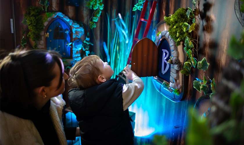 A boy opening the interactive wooden door as part of the multi sensory zones in our Lodge of Light.