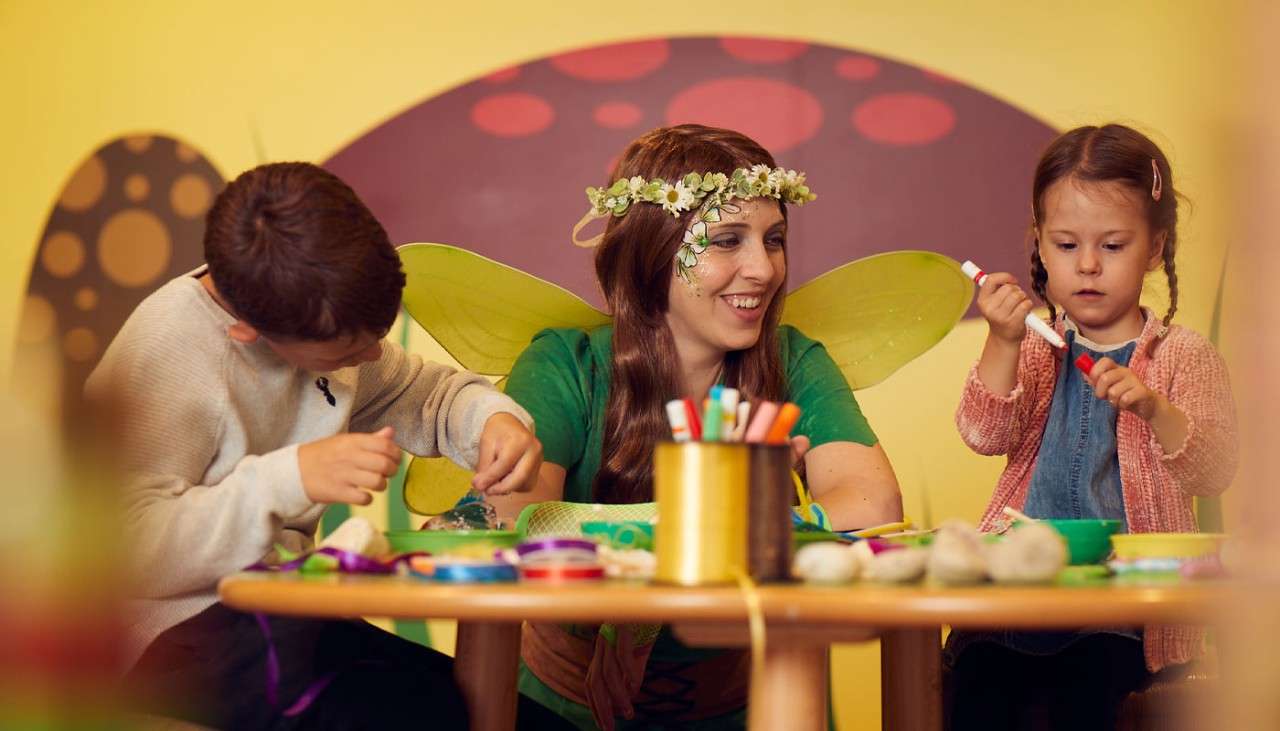 Young children sitting around a craft table with a fairy.