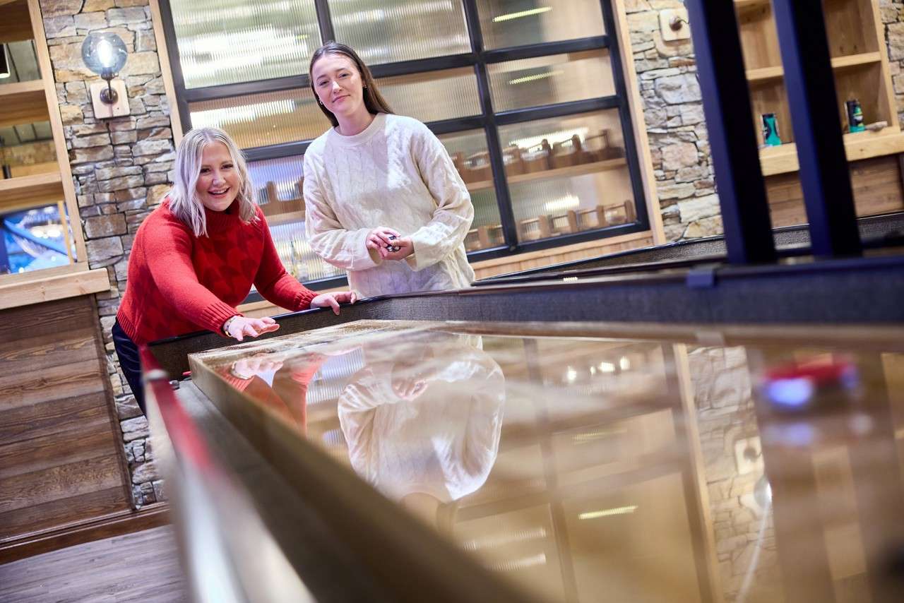 Two women playing a game of Shuffleboard.