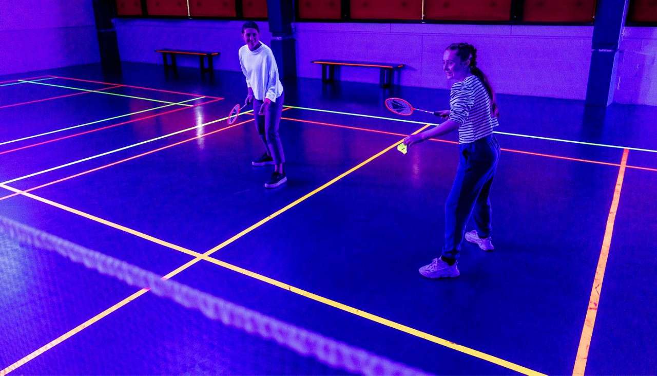 Two people playing badminton under UV lights