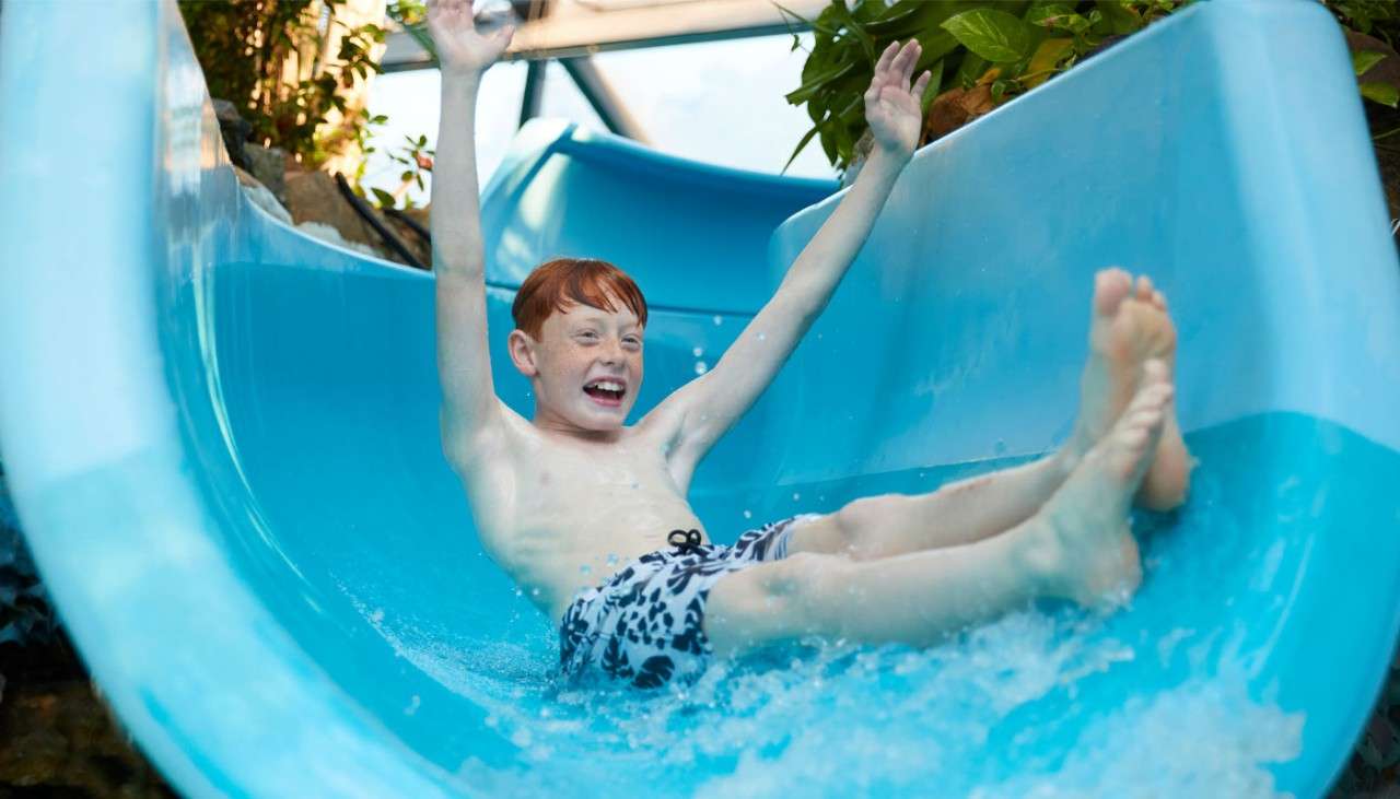 Young boy going down a water slide with his arms in the air.