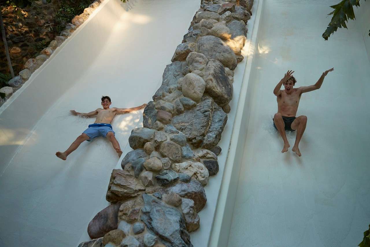 Two teenage boys sliding down a water piste slide. 